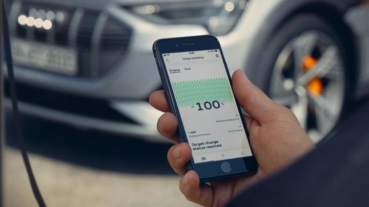 Man holding a smartphone with MyAudi app open in front of a silver Audi car