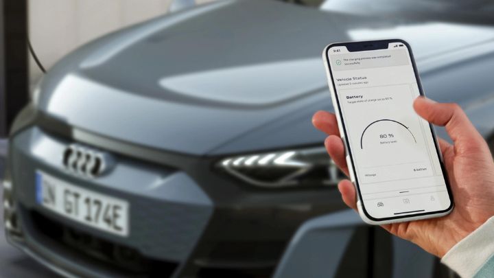 Man holding a smartphone with MyAudi app open in front of a grey Audi car