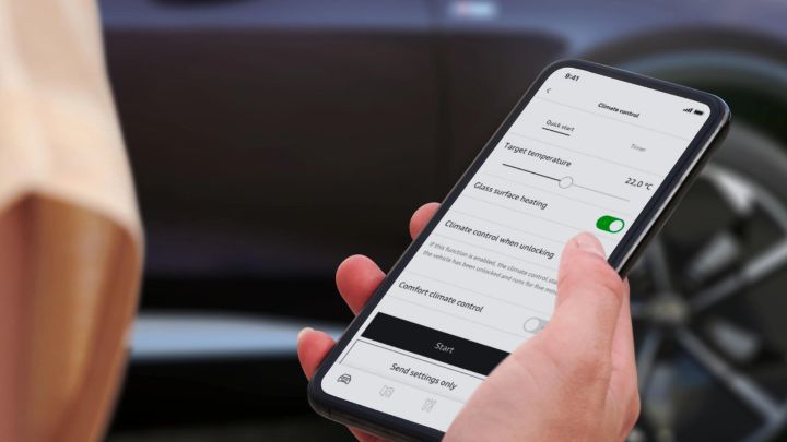 Man holding a smartphone with MyAudi app open in front of a black Audi car