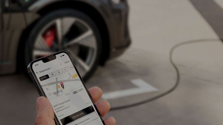 Man holding a smartphone with MyAudi app open in front of a black Audi car
