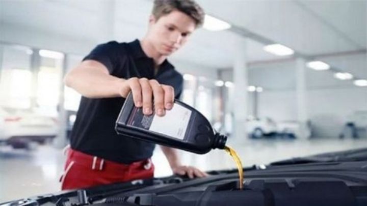 Man wearing black t-shirt and red trousers pouring oil into car