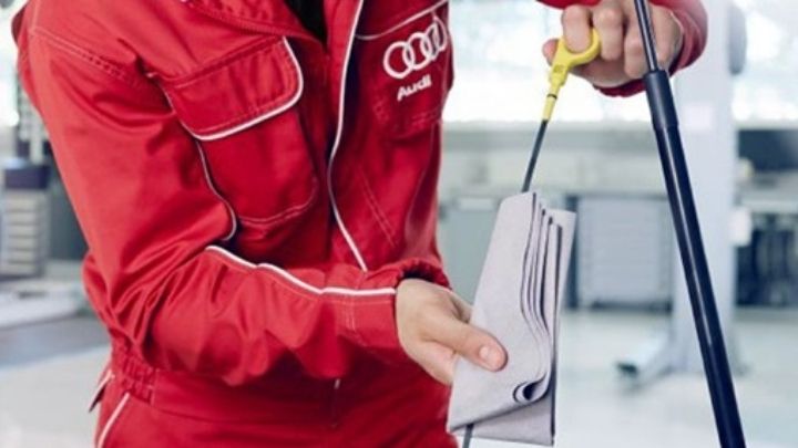 Man wearing red overalls with Audi's logo on the left pocket checking oil level