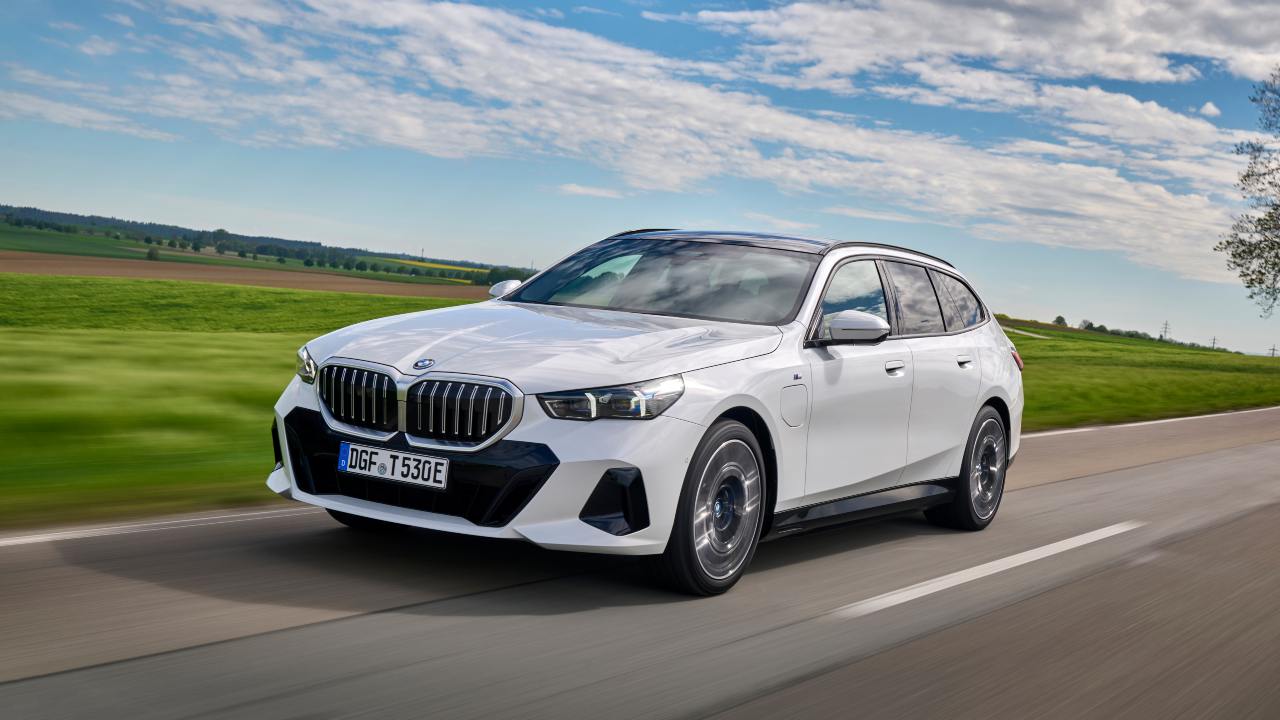 White BMW 5 Series Touring driving on a country road, front view