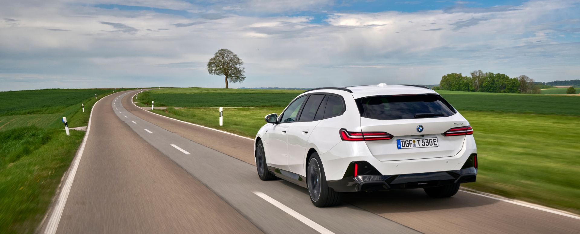 White BMW 5 Series Touring driving on a country road, rear view