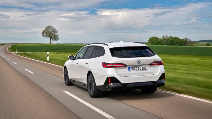 White BMW 5 Series Touring driving on a country road, rear view