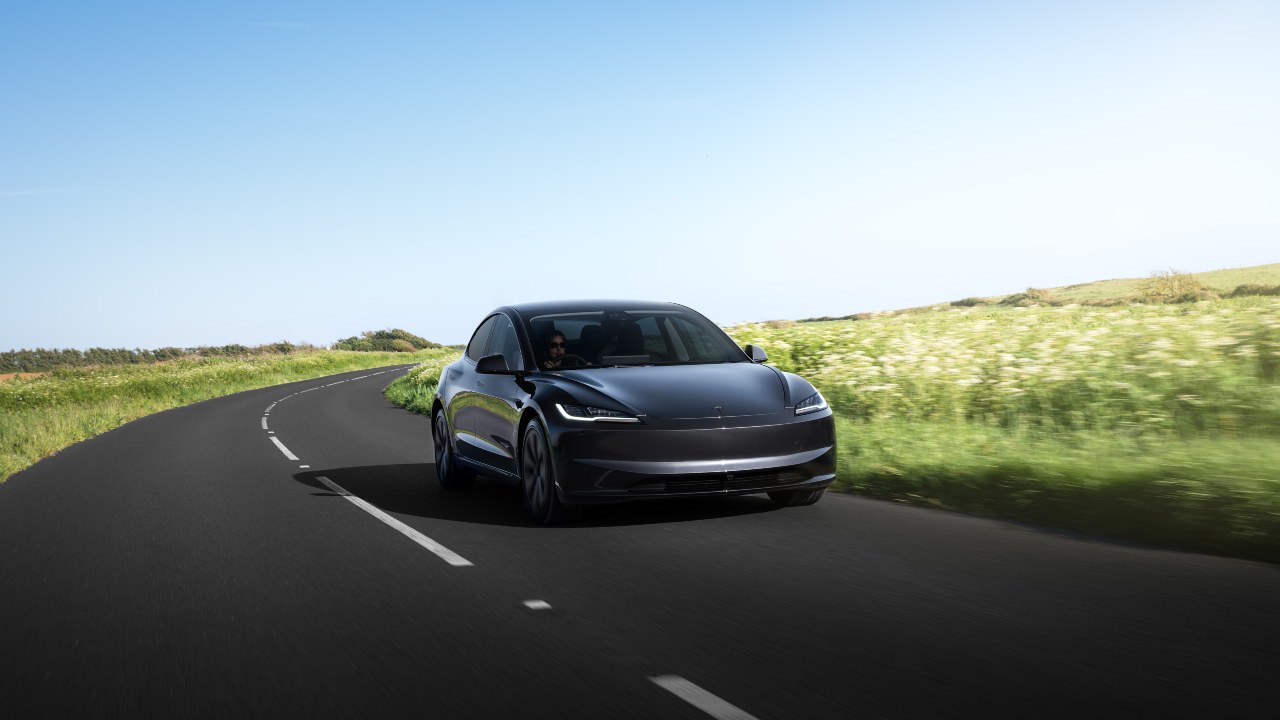 Tesla Model 3 driving along a winding country road on a sunny day