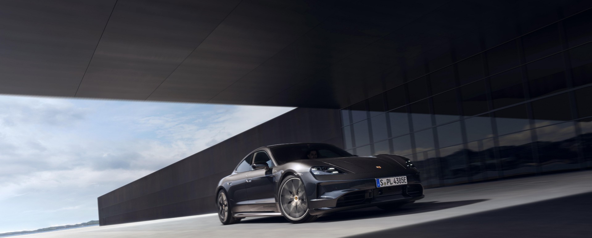 Black Porsche Taycan driving past a modern architectural building