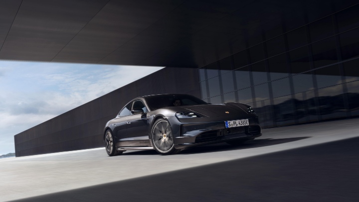 Black Porsche Taycan driving past a modern architectural building