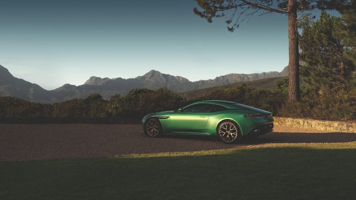 Green Aston Martin DB12 grand tourer shown in side profile against a mountainous landscape
