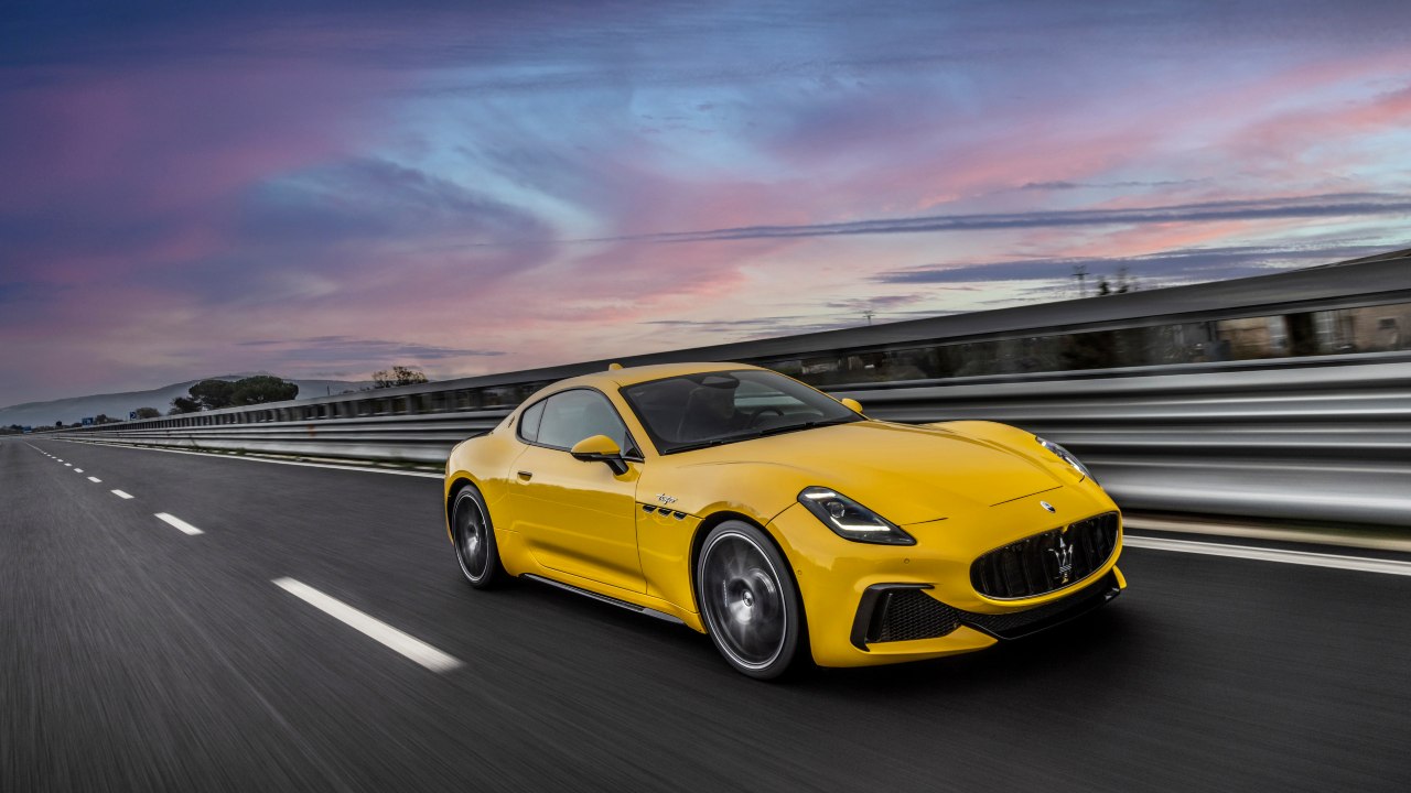 Yellow Maserati GranTurismo sports car driving on an open road at sunset