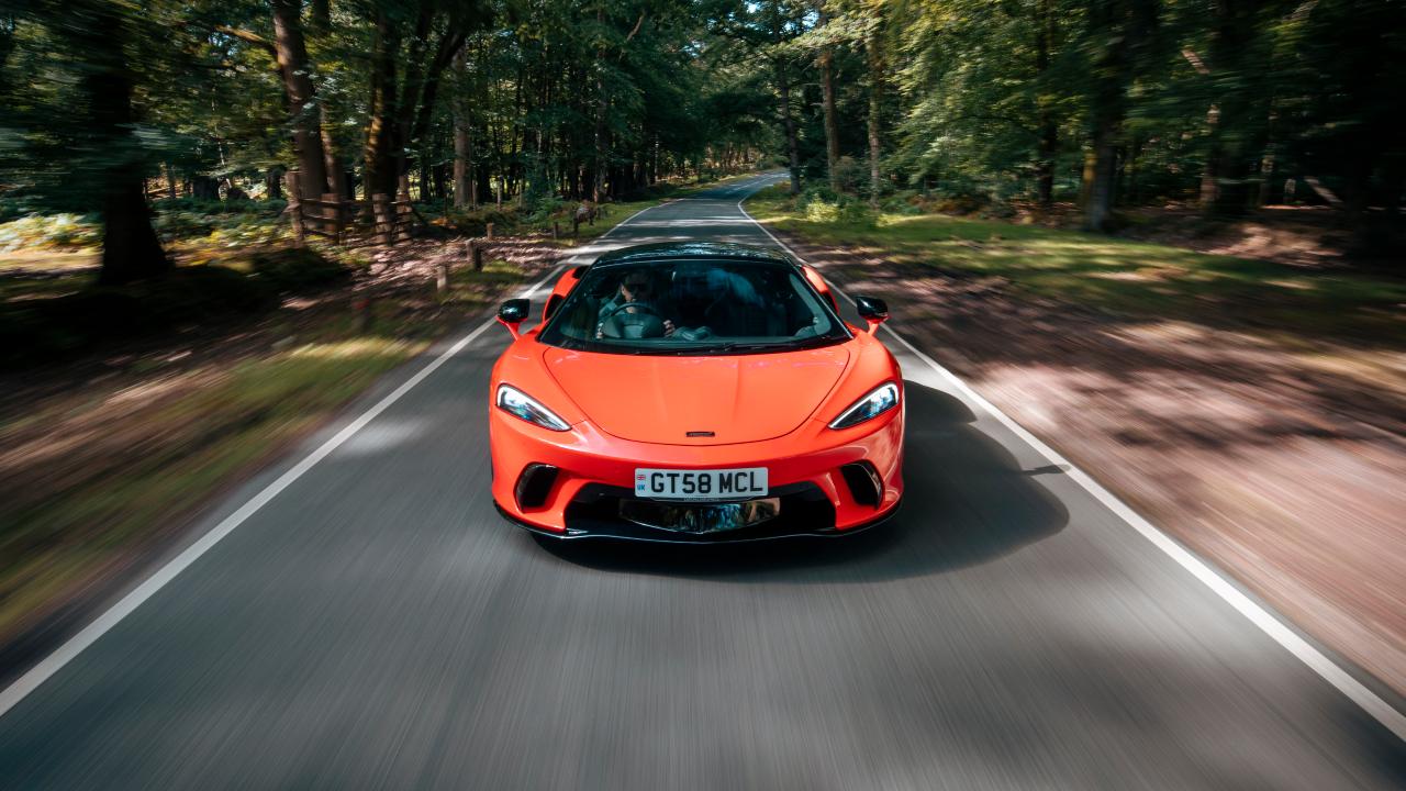 McLaren GTS supercar driving head‑on along a tree‑lined road