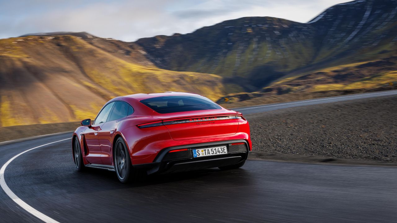Red Porsche Taycan electric saloon driving on a winding mountain road from a rear three‑quarter view