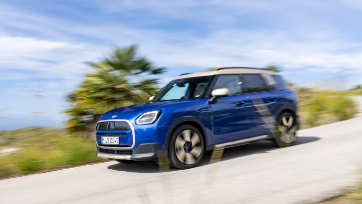 Blue MINI Countryman electric SUV driving from a front three‑quarter angle on a country road