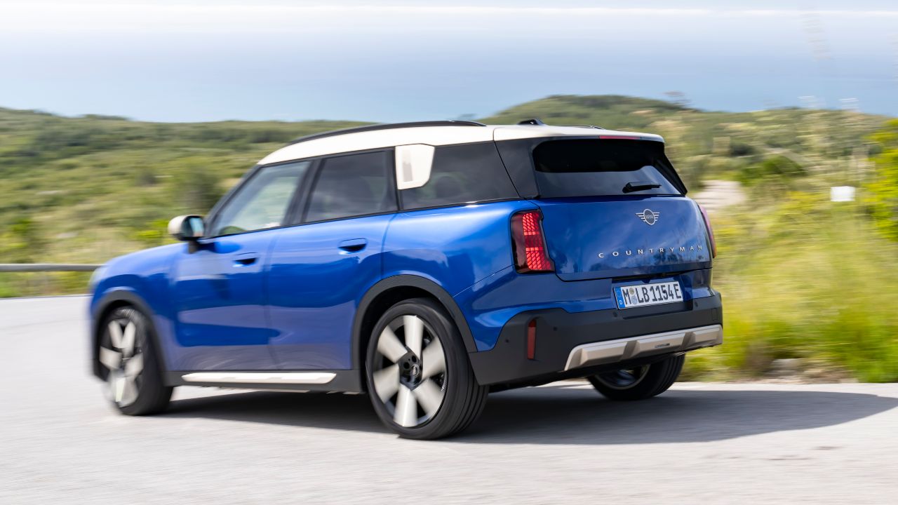 Blue MINI Countryman electric SUV driving from a rear three‑quarter view on a winding road