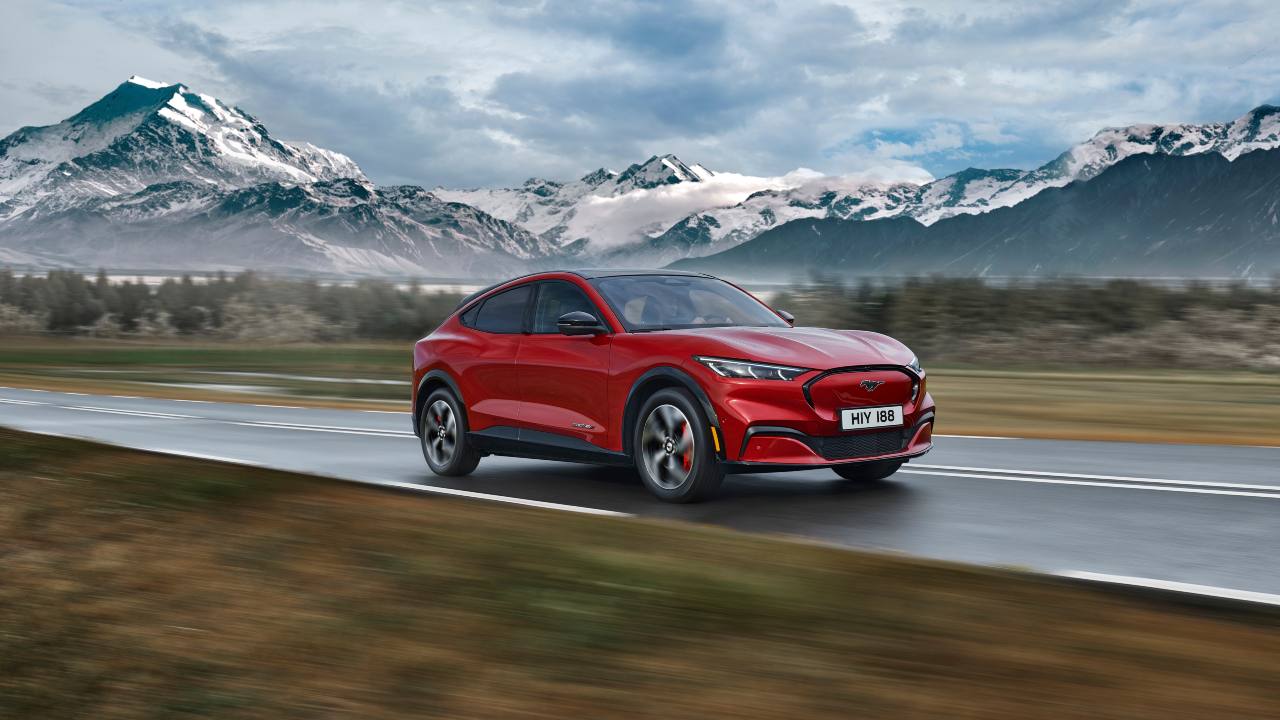 Red Ford Mustang Mach‑E electric SUV driving on an open road with mountains in the background