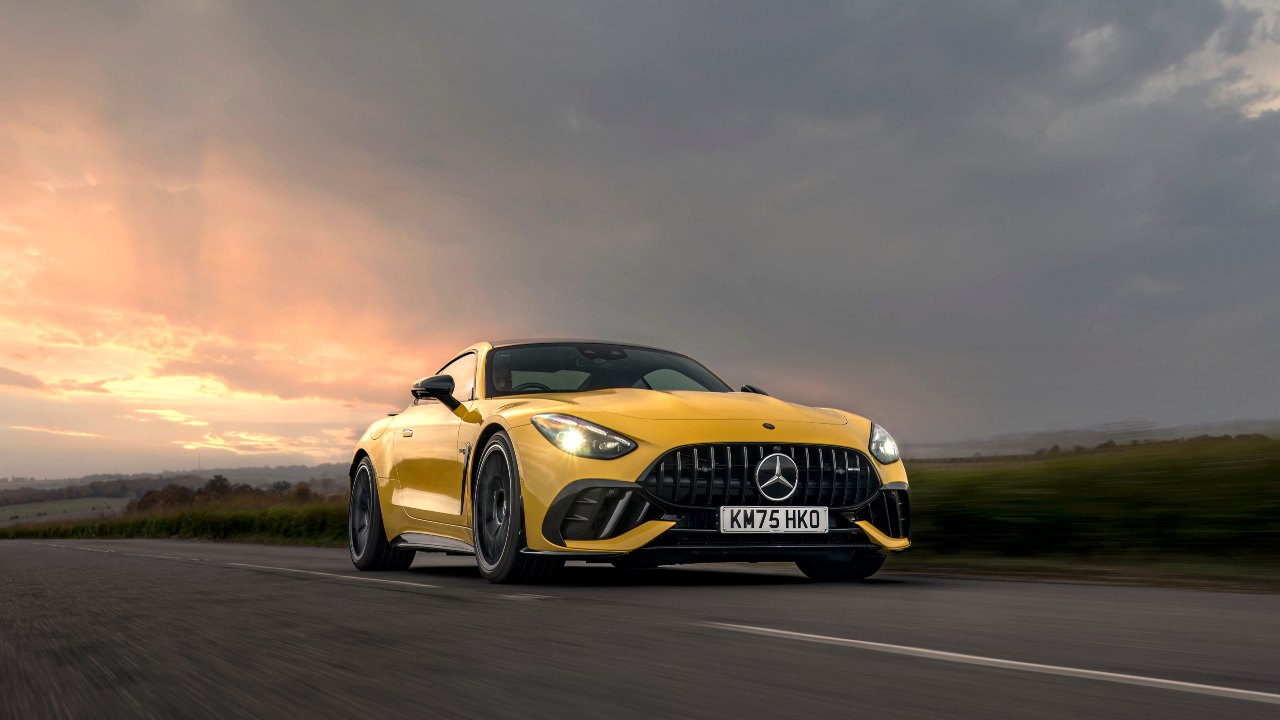 Yellow Mercedes-AMG GT driving on open road at sunset, front three-quarter view