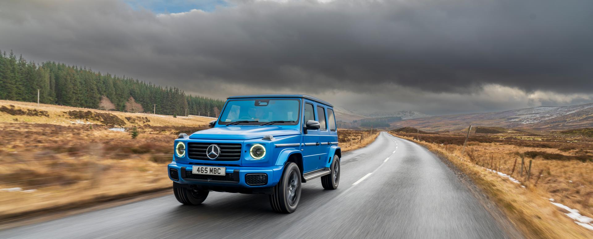 Blue Mercedes-Benz G-Class driving on rural road, front three-quarter view
