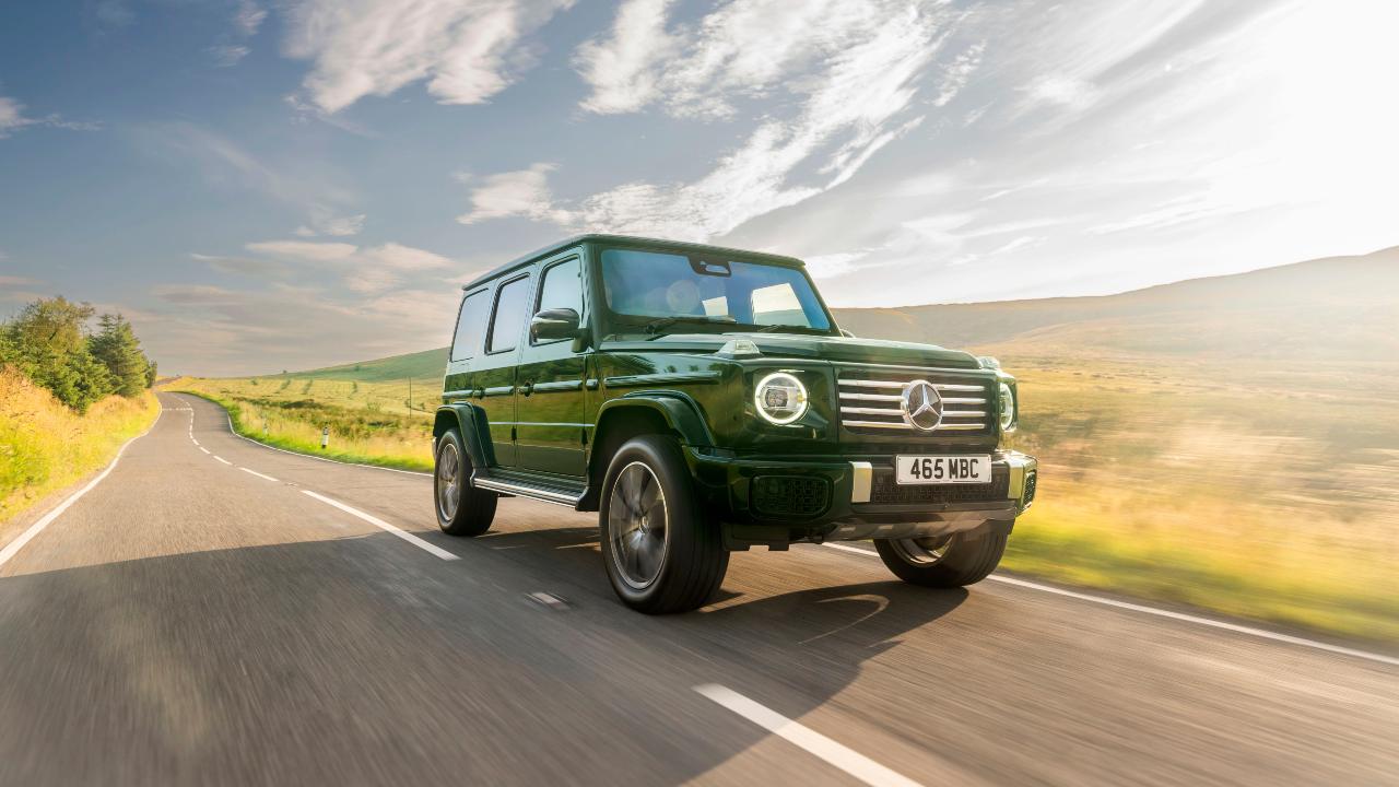 Green Mercedes-Benz G-Class driving through countryside, front three-quarter view
