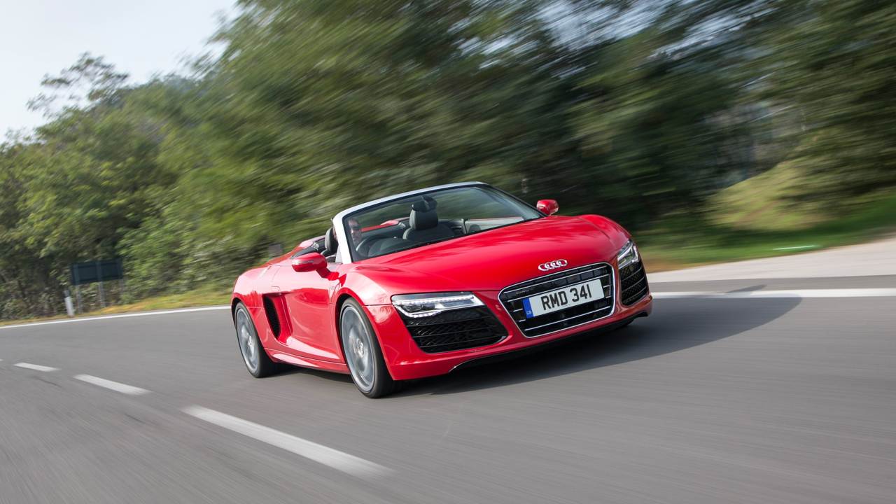 Red Audi R8 Spyder convertible supercar driving on a tree-lined country road