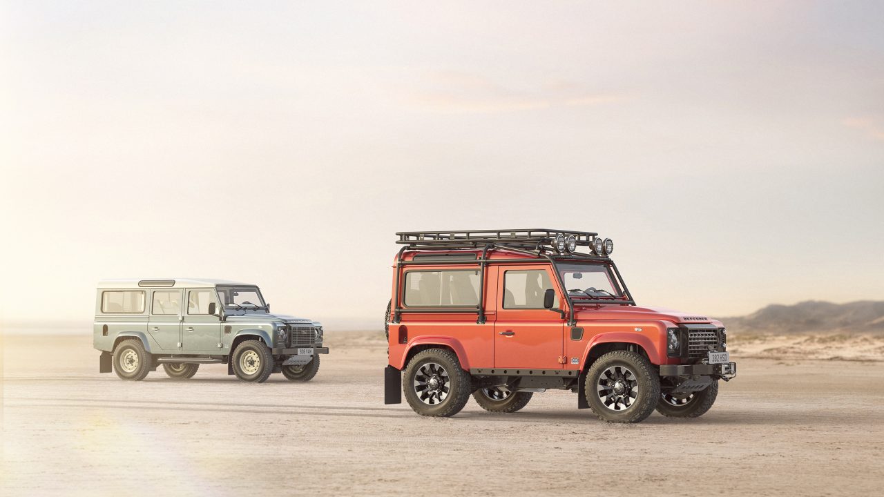 Silver and orange Land Rover Defender models parked together on a desert landscape