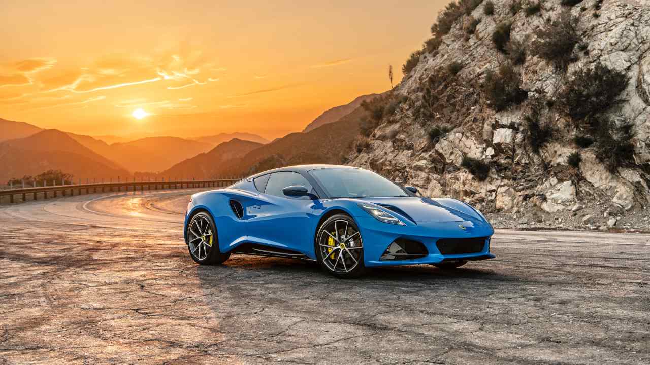 Blue Lotus Emira sports car driving on a mountain road at sunset