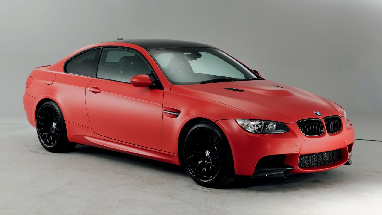Red BMW M3 Coupe (E92) with black roof and alloy wheels shown in a studio setting