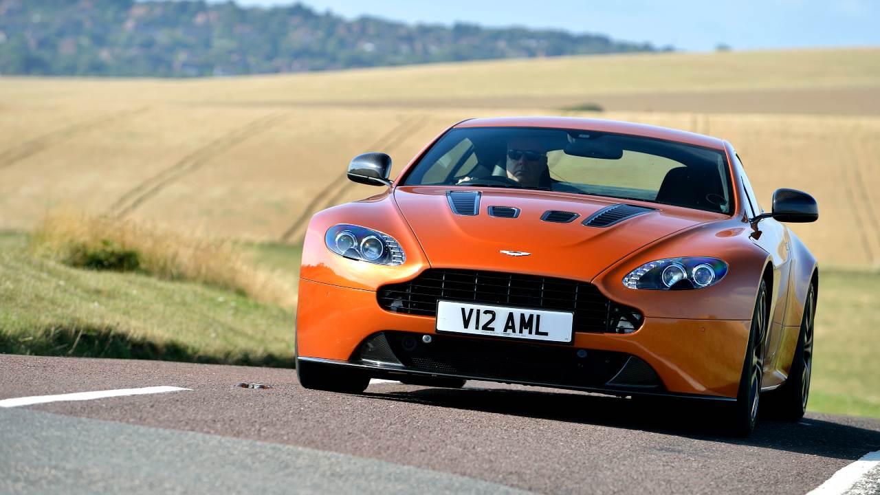Orange Aston Martin V12 Vantage sports car driving on a rural countryside road