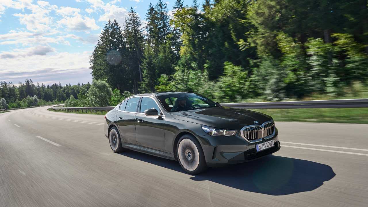 Black BMW 5 Series saloon driving along a tree-lined road