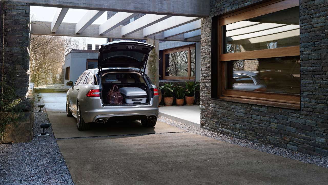 Silver Jaguar XF estate with boot open outside modern house