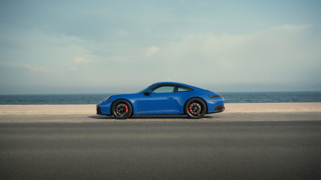Blue Porsche 911 side profile parked beside seafront promenade
