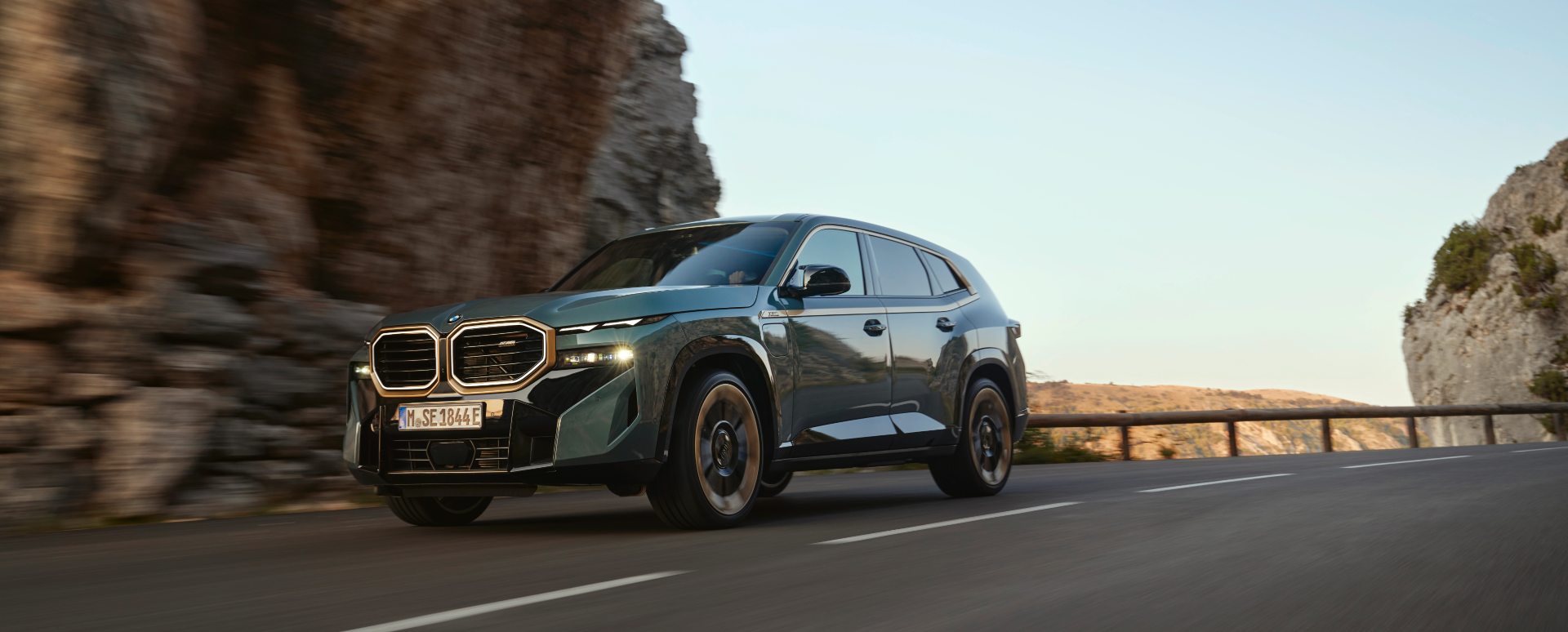 BMW XM driving through mountain pass, front three-quarter view with motion blur