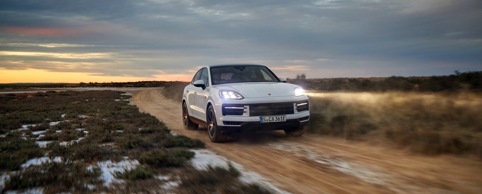 Porsche Cayenne E-Hybrid driving on a dirt road at dusk with dust trailing