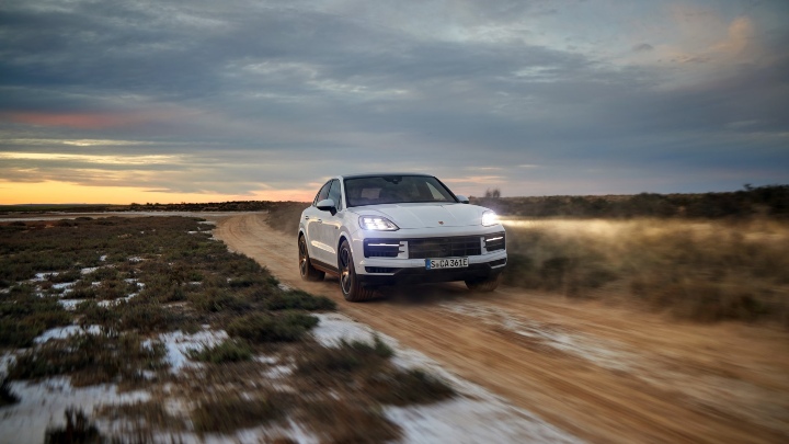 Porsche Cayenne E-Hybrid driving on a dirt road at dusk with dust trailing