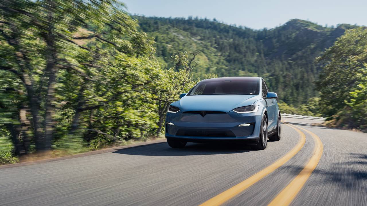 Tesla Model X driving on a winding mountain road surrounded by greenery