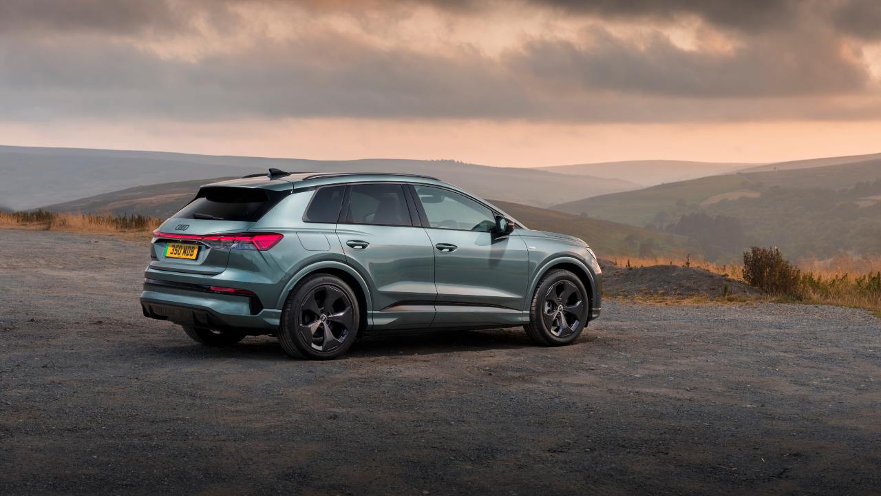 Audi Q4 electric SUV rear side view parked on a gravel road overlooking rolling hills at sunset