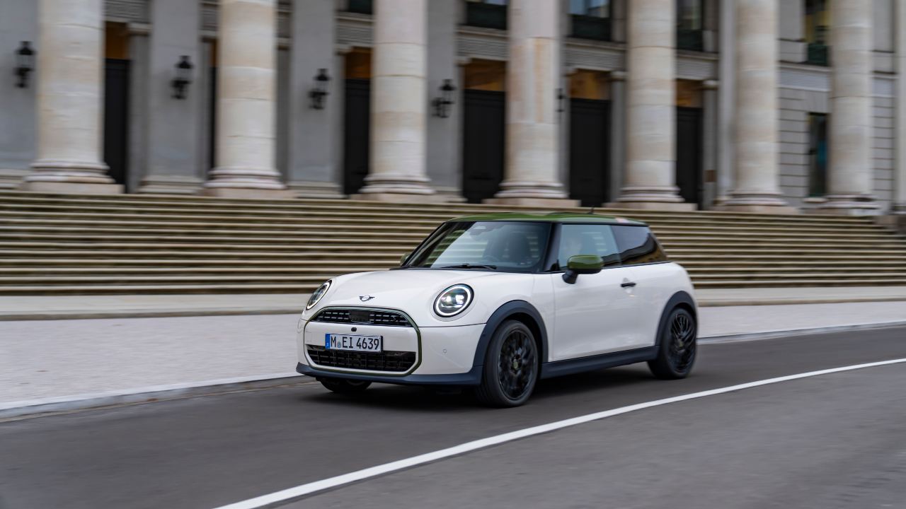 White Mini Cooper with contrast roof driving past a historic columned building