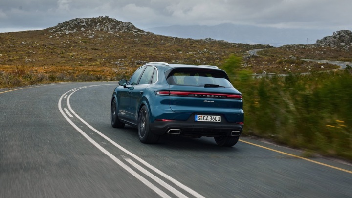 Porsche Cayenne SUV driving away on a winding rural road, rear three‑quarter view