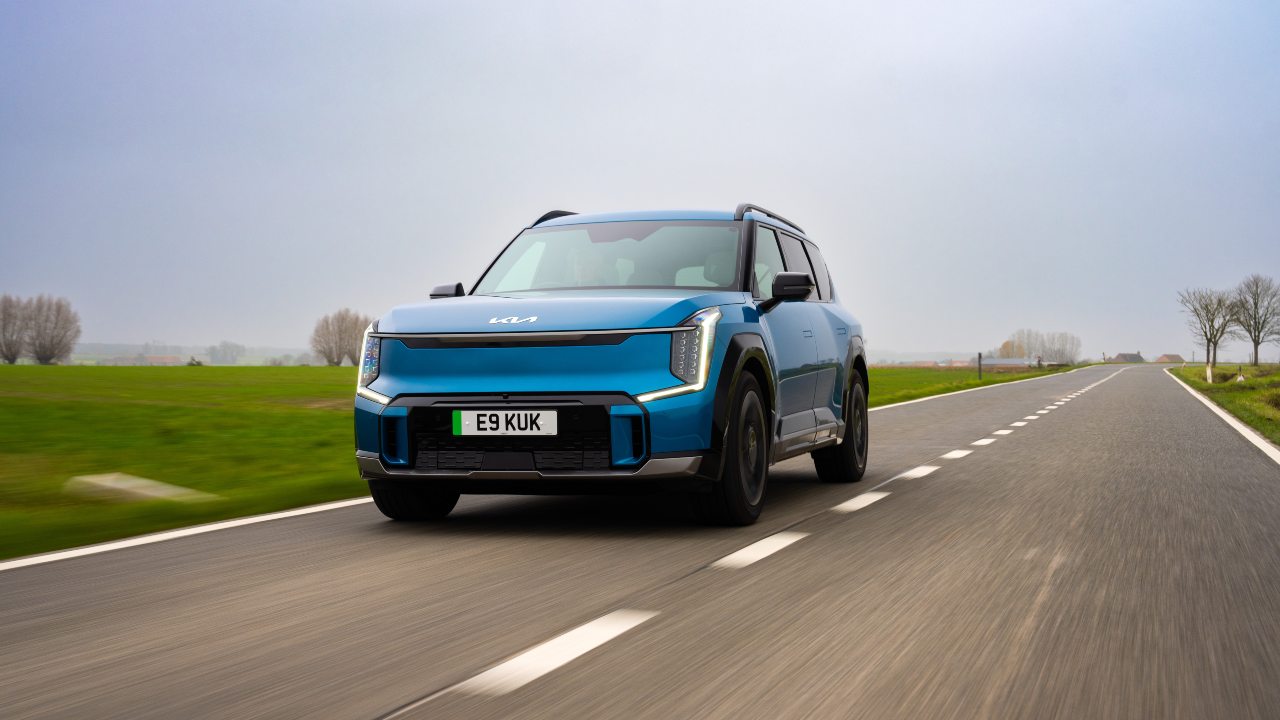 Kia EV9 electric SUV driving on a rural road from a front three‑quarter angle
