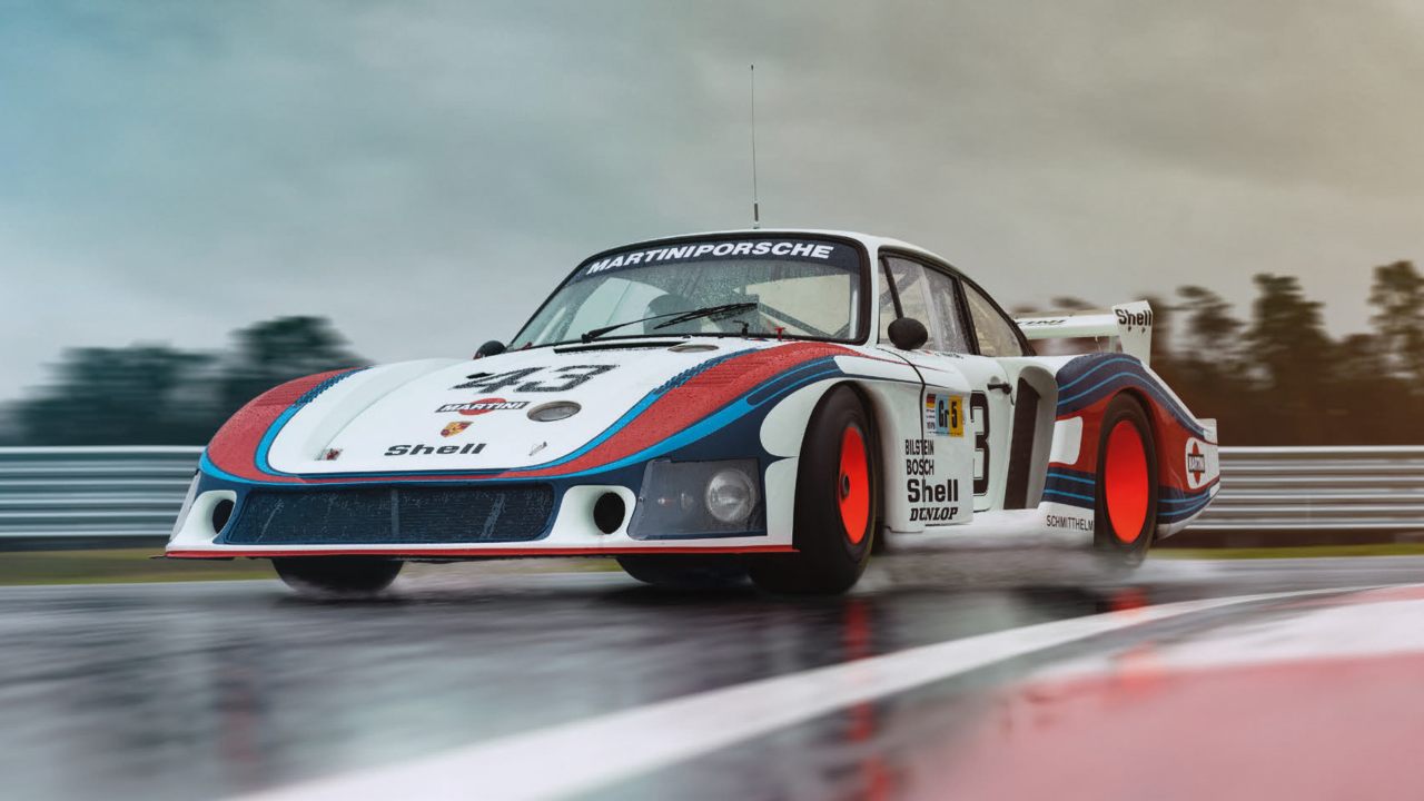 Classic Porsche 935 race car in Martini livery driving on wet track with spray