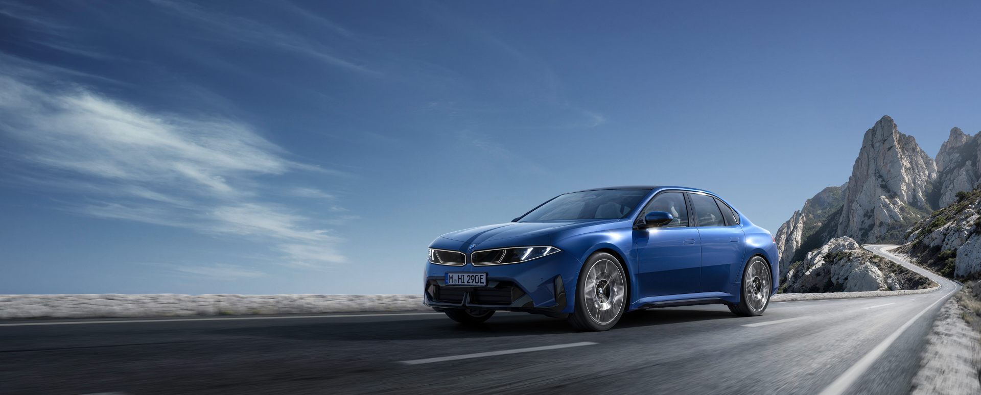 Blue BMW i3 driving along a scenic mountain road with rocky cliffs in the background