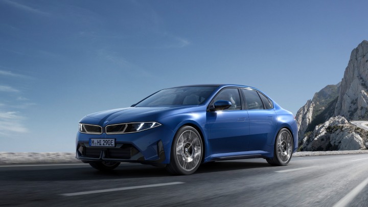 Blue BMW i3 driving along a scenic mountain road with rocky cliffs in the background