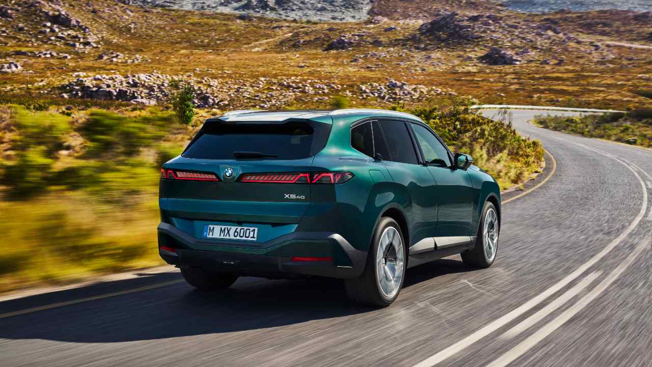 Rear three-quarter view of a green BMW X5 driving on a countryside road