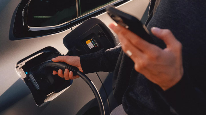 Close up of a person plugging the i4 into a charger whilst using the My BMW app