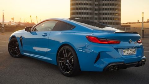 A blue BMW M8 Competition parked on the road with a round building in front of it