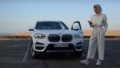 woman standing in front of bmw x1 using my bmw smartphone app