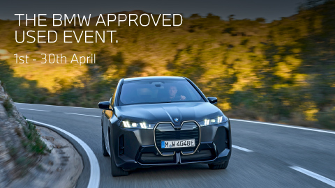 Front shot of black BMW vehicle driving on a road surrounded by trees. Promotional text overlay.