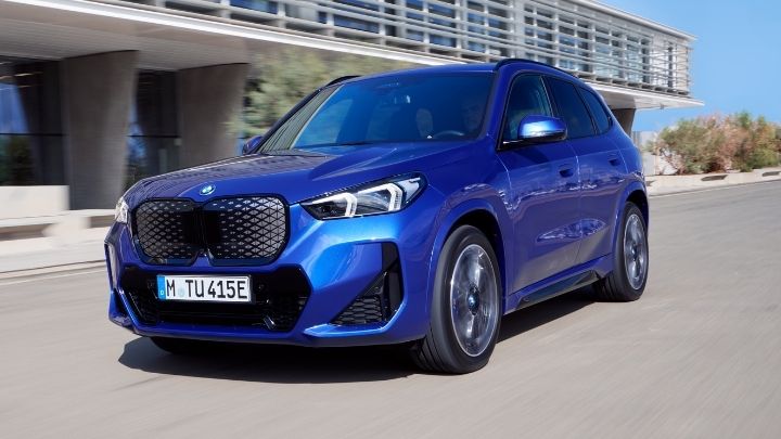 Blue BMW driving in front of a modern building