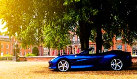 Blue Ferrari parked outside under the trees.
