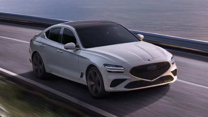 White Genesis G70 driving down a road at sunset