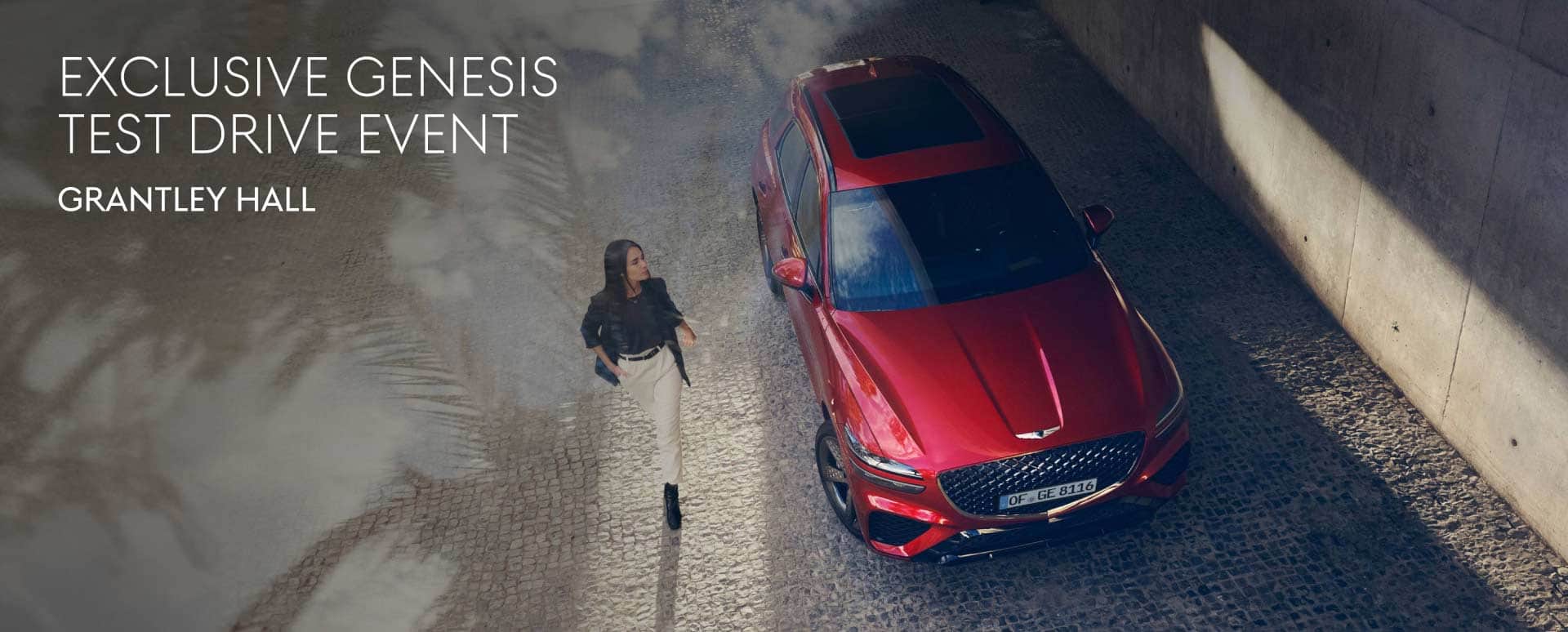 A red Genesis car photographed from above. Parked in a quiet area with a woman walking beside it.